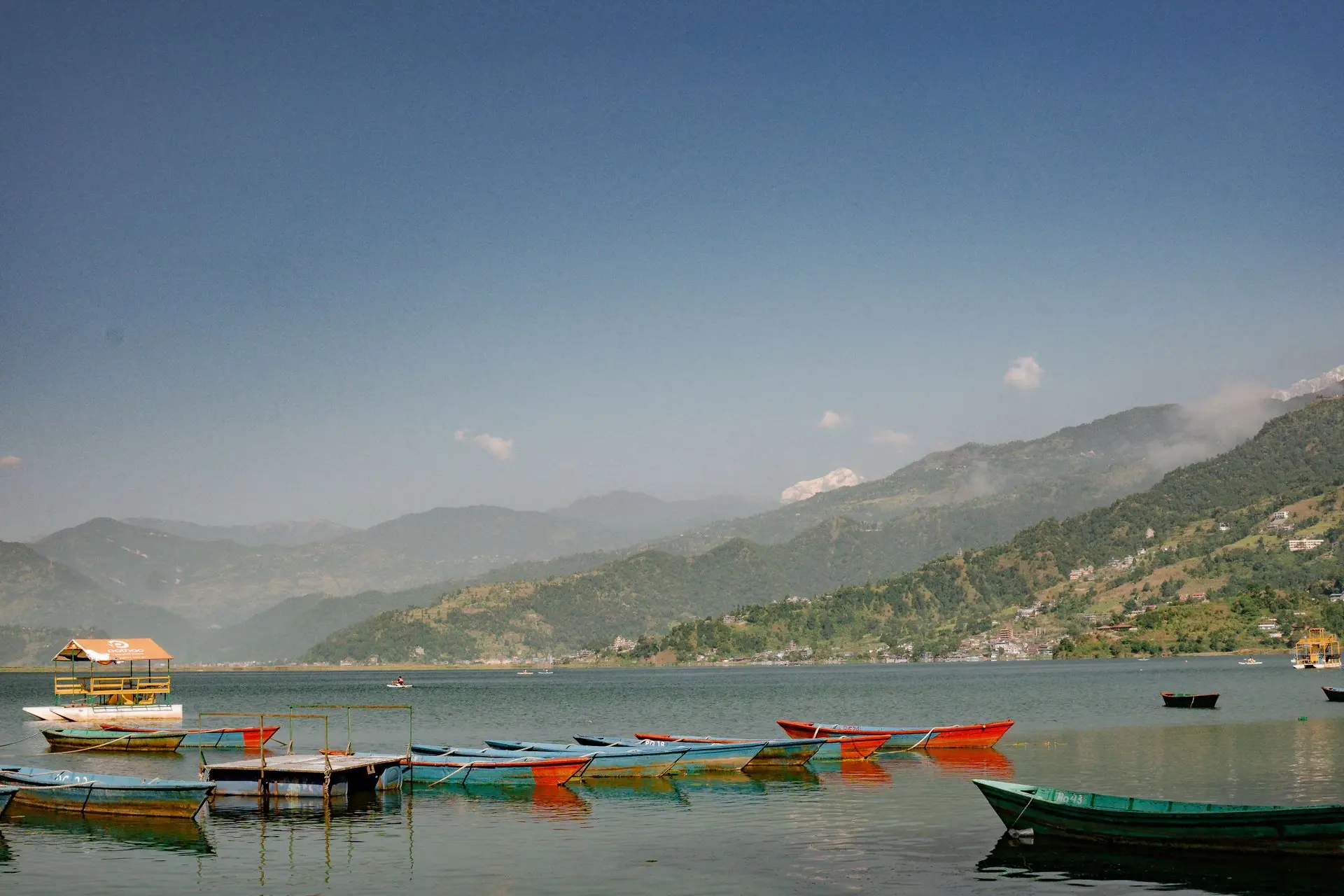 Boats on Phewa Lake with hillside communities and mountains beyond, Pokhara, Nepal.